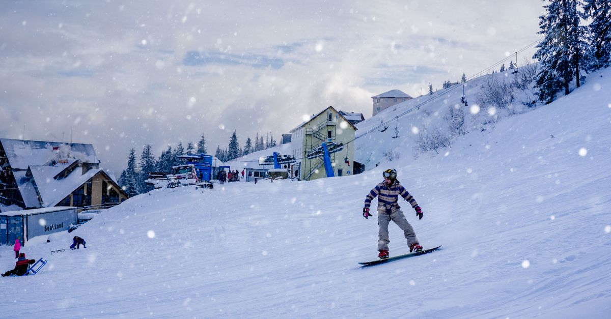A snowboarder glides down a snowy slope at a ski resort in Romania, surrounded by winter beauty.